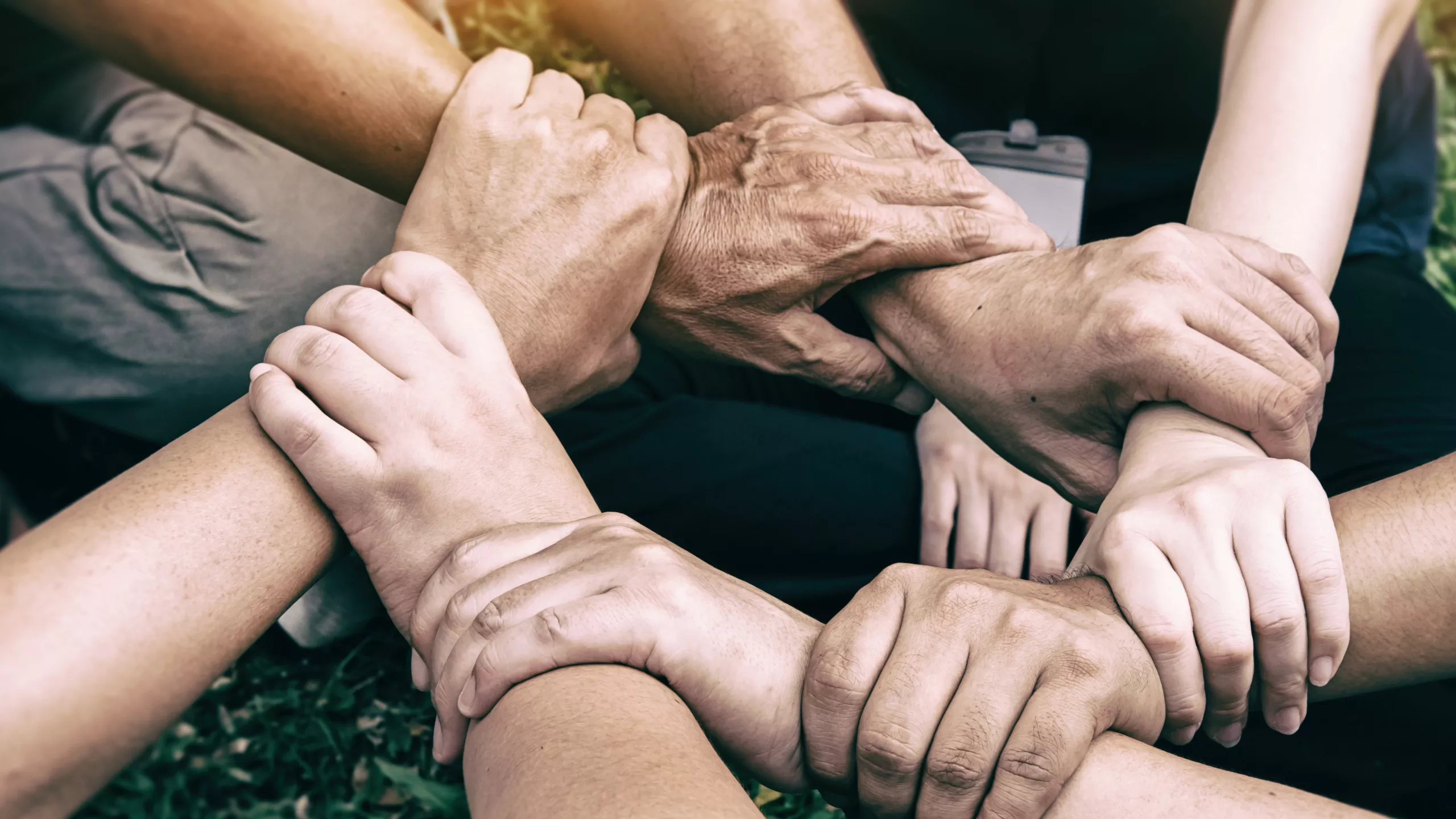 W kadrze widzimy dłonie i przedramiona 7 osób, symbolizujące współpracę na rzecz wspólnego działania